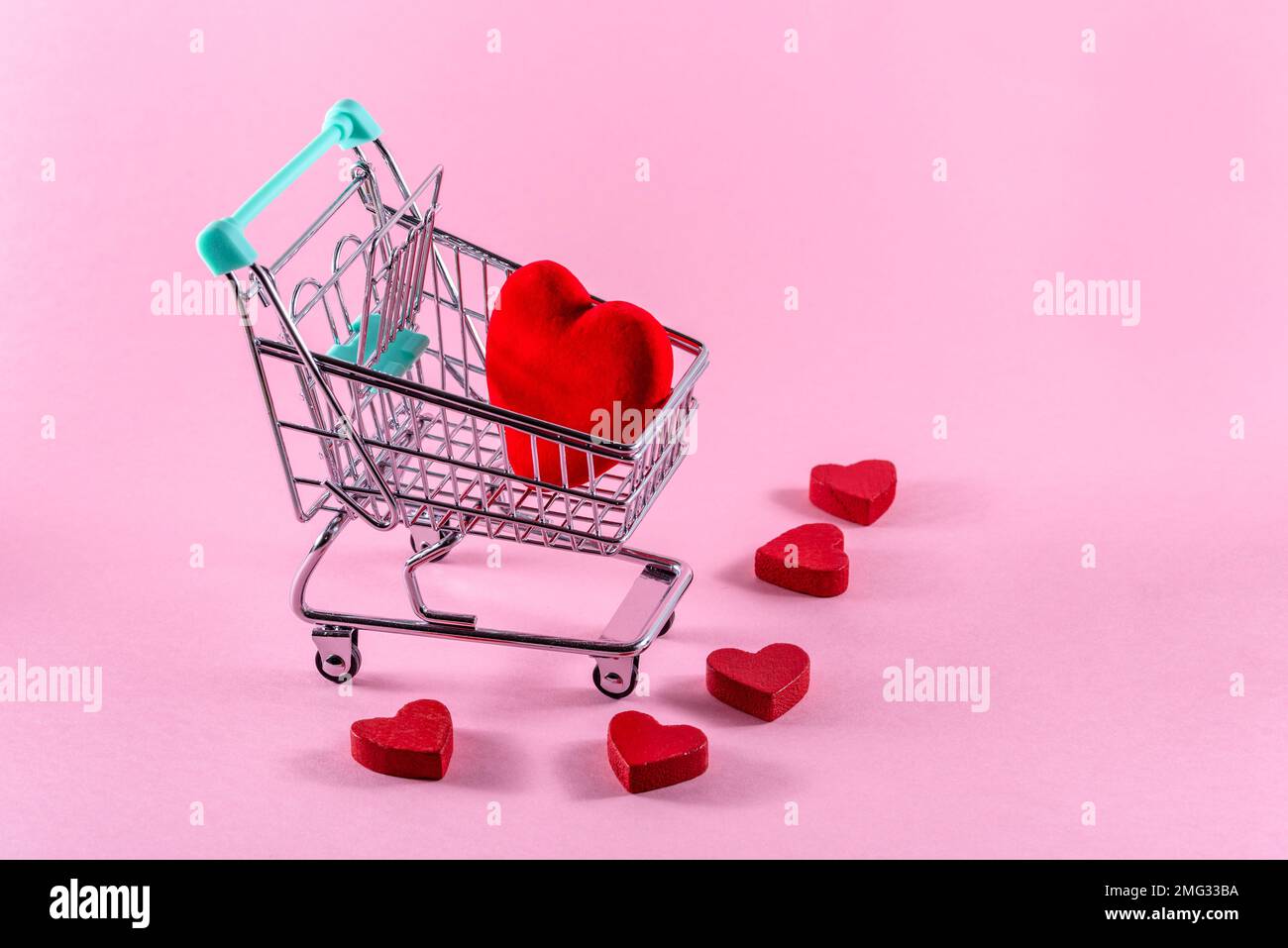 Cuore rosso su un piccolo carrello per lo shopping su sfondo rosa. Concetto di shopping di San Valentino. Spazio di copia. Foto Stock