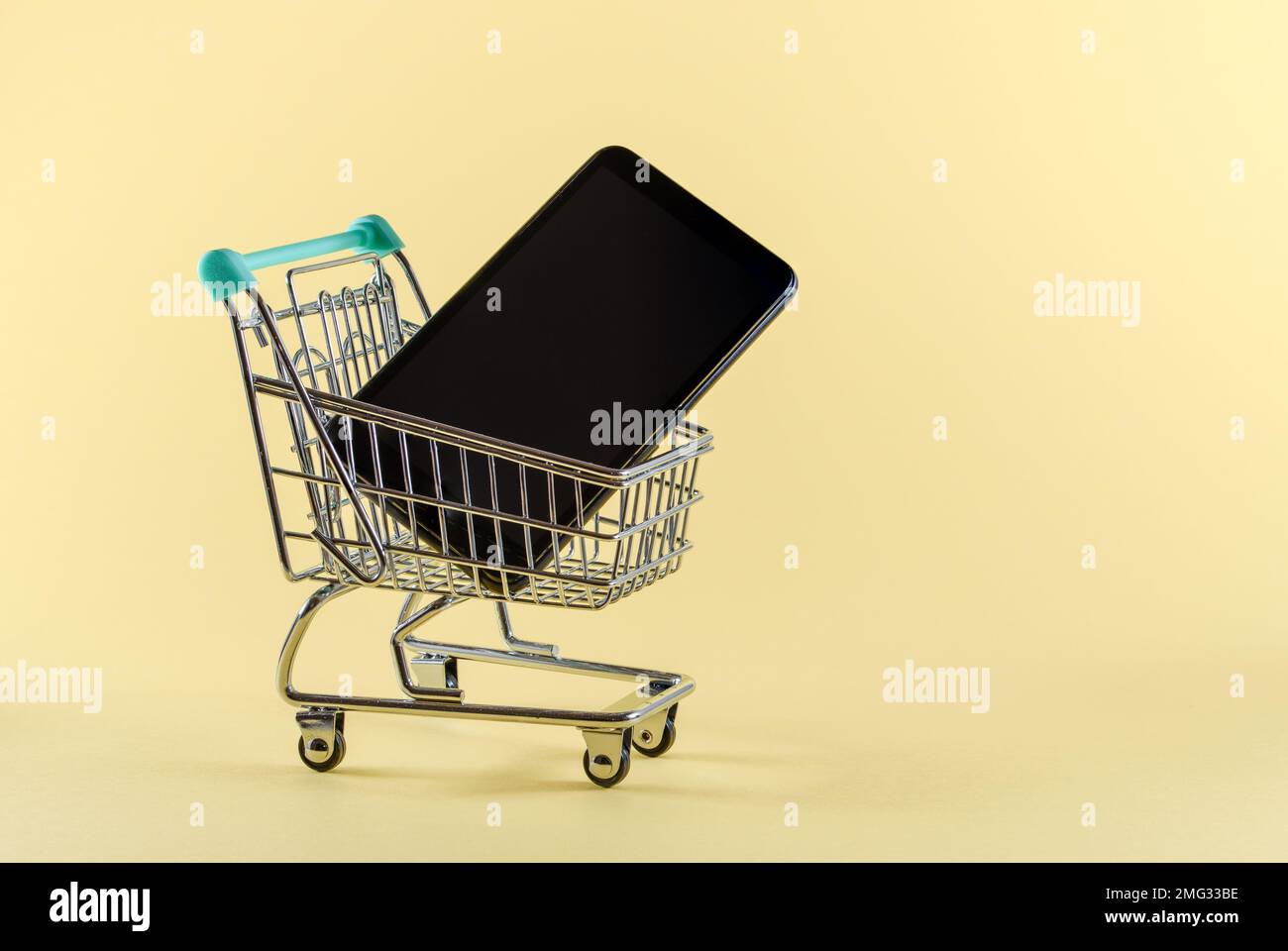 Smartphone in un piccolo carrello di shopping agaist uno sfondo giallo chiaro. Shopping online concept.Copy spazio. Foto Stock