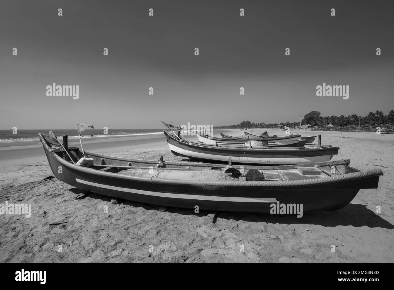 Paesaggio a Goa, Karnataka o Kerala con barche da pesca sulla costa e persone in lontananza sulla spiaggia di sabbia. Le donne indiane nuotano in un vestito Foto Stock