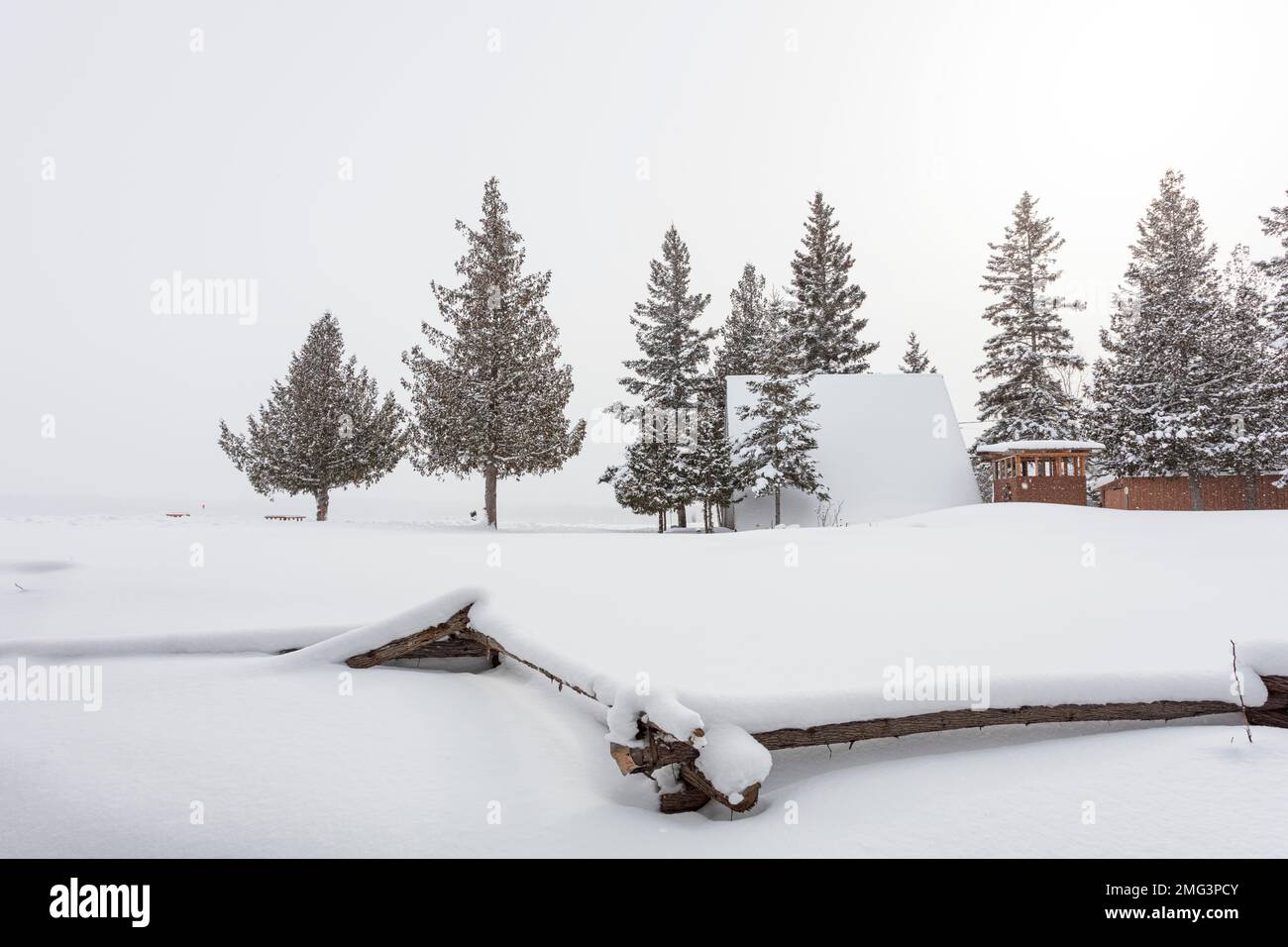 Una struttura A-frame sull'isola di Manitoulin (Ontario, Canada) con una recinzione in primo piano a doppia rotaia quasi completamente coperta di neve. Foto Stock