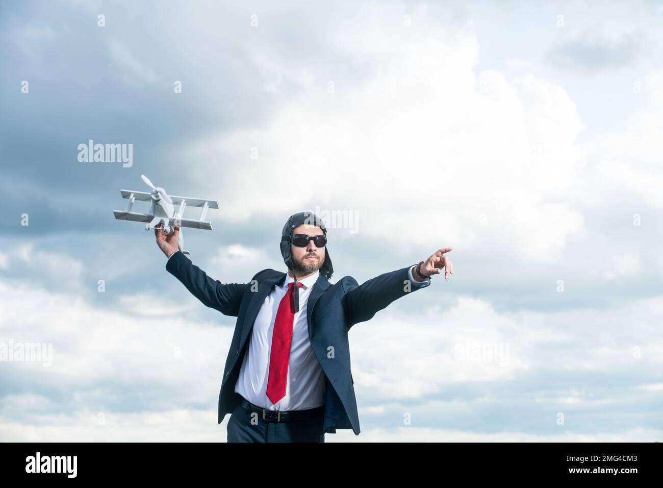 uomo d'affari in tuta e cappello pilota lancio aereo giocattolo su sfondo cielo. opportunità Foto Stock