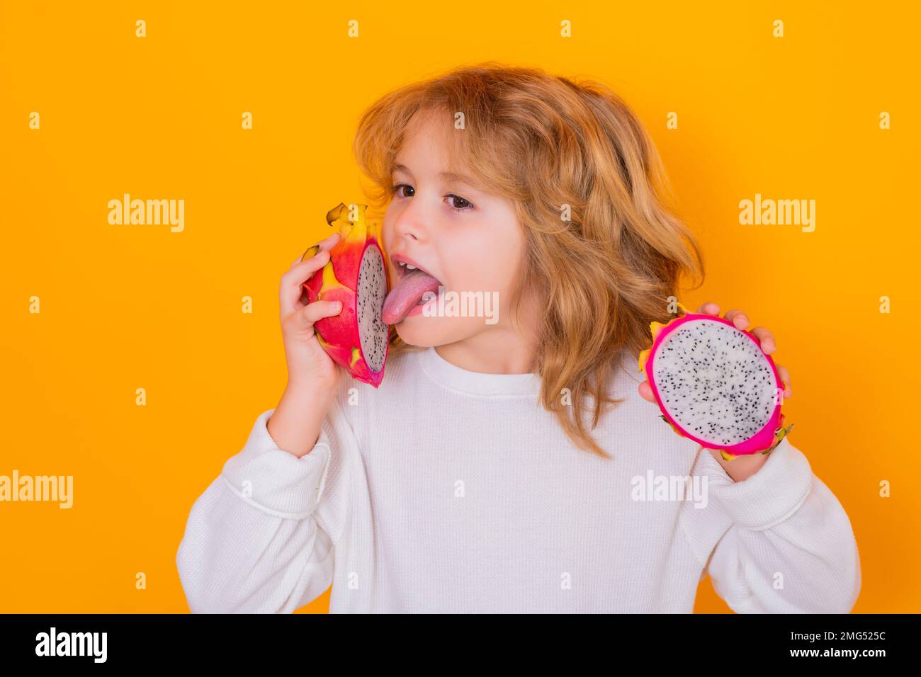 I bambini mangiano frutta di drago in studio. Studio ritratto di carino bambino con frutto drago isolato su sfondo giallo. Foto Stock