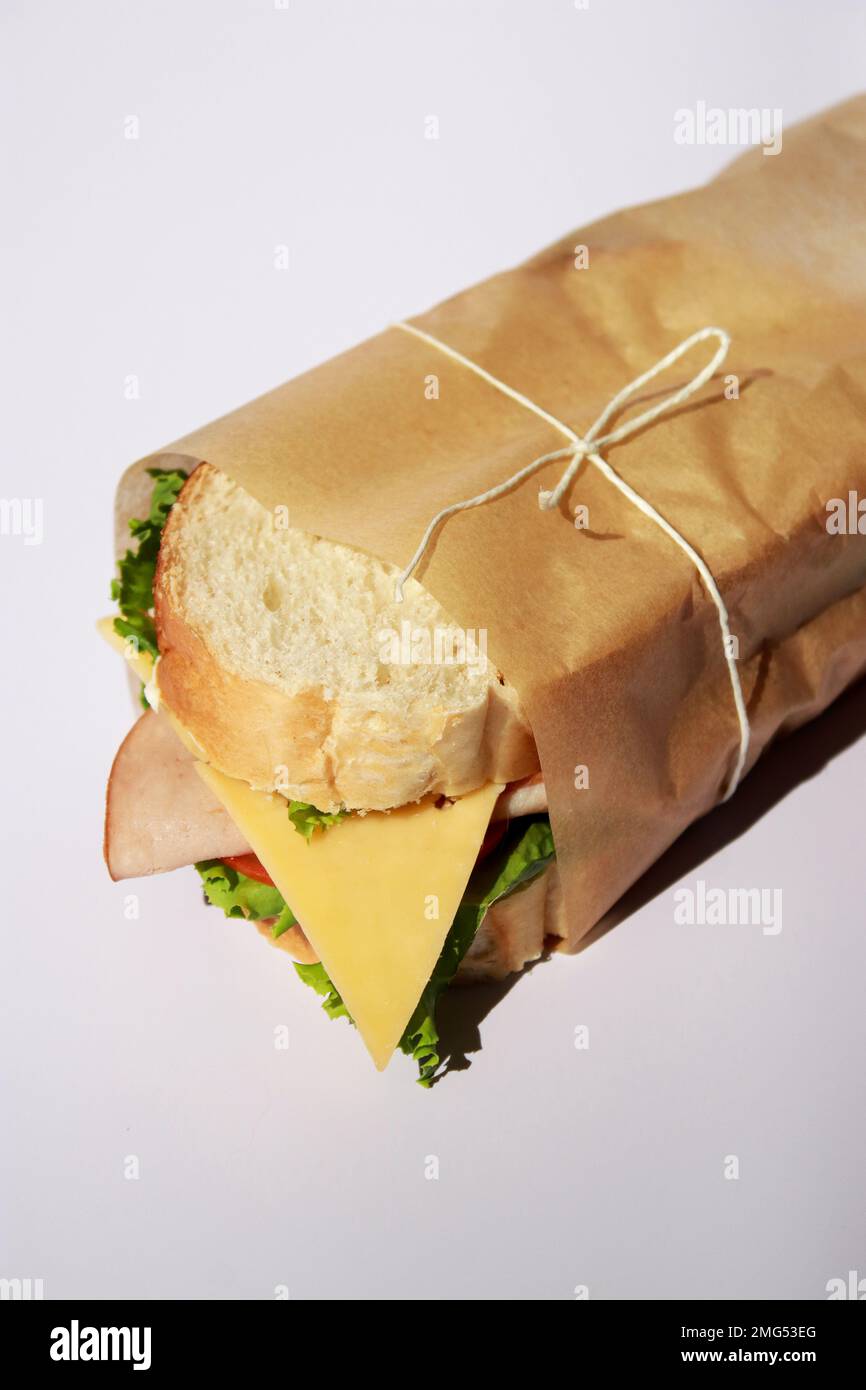 Panino di formaggio e prosciutto avvolto in carta su sfondo bianco con spazio copia Foto Stock