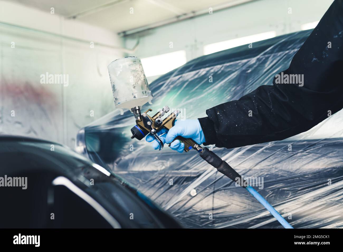 Persona che indossa guanti protettivi in uniforme e blu verniciatura di parti scoperte dell'auto con aerografo. Verniciatura auto. Scatto orizzontale in interni. Foto di alta qualità Foto Stock