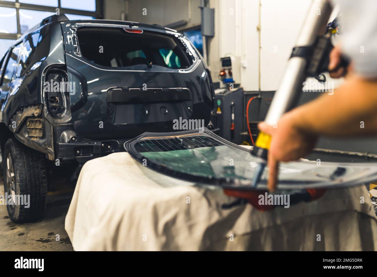 Vista posteriore dell'uomo che applica adesivo industriale al vetro del finestrino da installare sul retro dell'auto. Lavori in garage. Concentrarsi sullo sfondo. Scatto orizzontale in interni. Foto di alta qualità Foto Stock