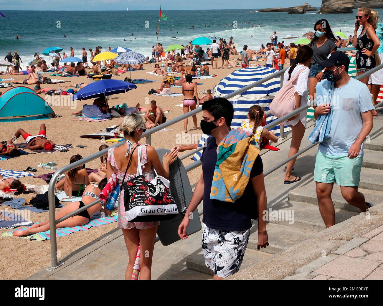 People wearing face masks at the beach in Biarritz, southwestern France, Monday July 3, 2020, as several sites around France have started requiring masks outdoors in recent days. Starting Monday, 69 towns in the Mayenne region of western France imposed outdoor mask rules, as did parts of the northern city of Lille and coastal city of Biarritz in French Basque country. (AP Photo/Bob Edme) Foto Stock