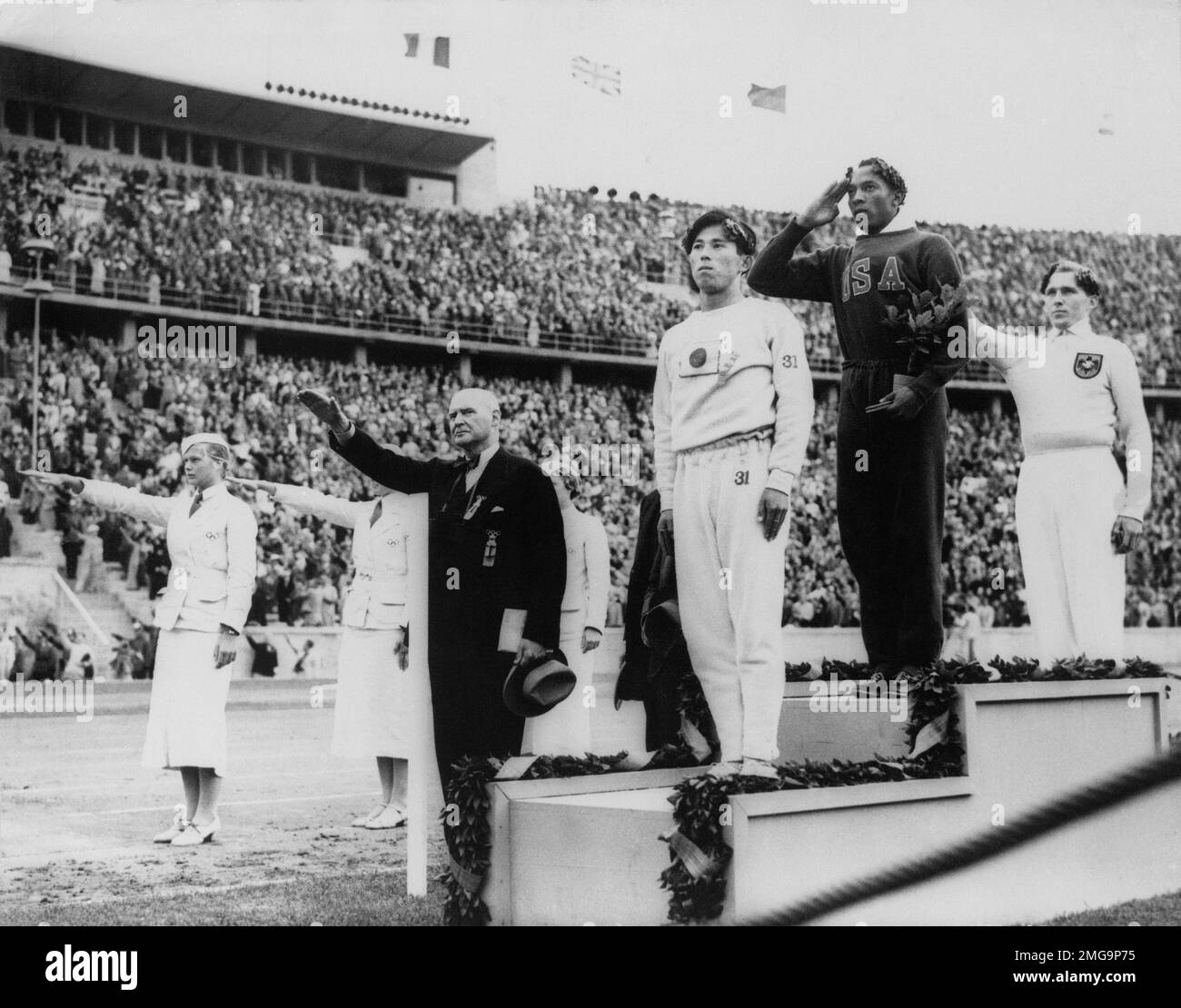 FILE - In this Aug. 11, 1936, file photo, America's Jesse Owens, second from right, salutes during the presentation of his gold medal for the long jump, after defeating Nazi Germany's Lutz Long, right, during the 1936 Summer Olympics in Berlin. Naoto Tajima of Japan, center, placed third. The performance of Jesse Owens will be honored in the stadium where he won four gold medals at the 1936 Olympic Games when the world championships are held in Berlin this month. (AP Photo/File) Foto Stock