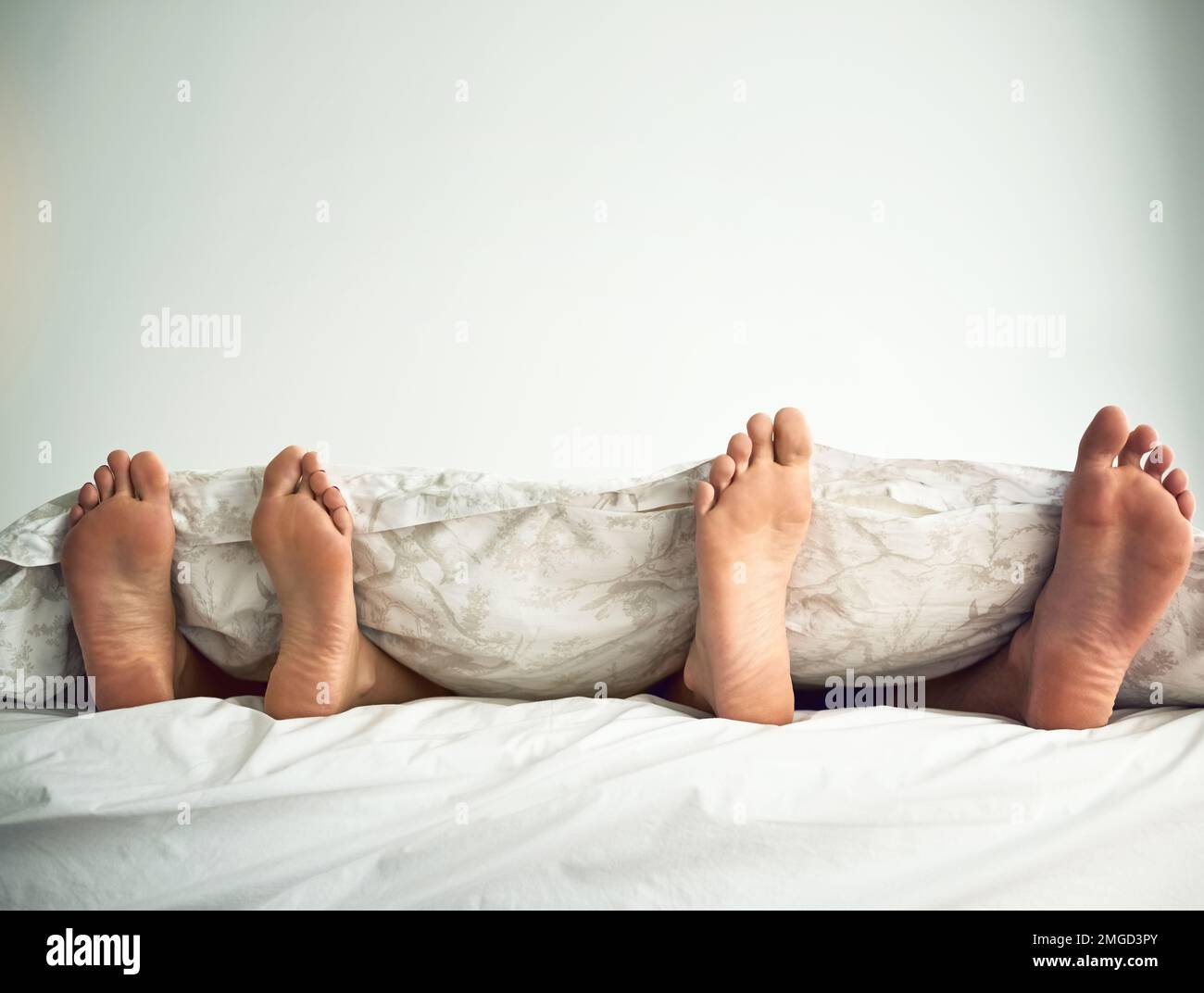 Lascia annullare oggi e rimanere a letto. un paio di piedi che si scopano da sotto le lenzuola. Foto Stock