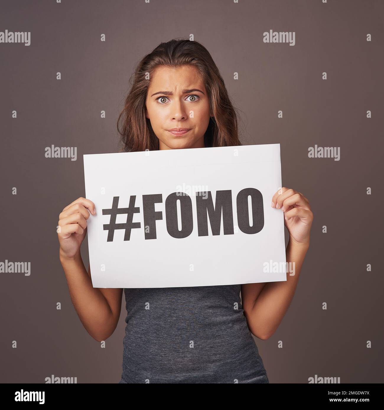 Da qualche parte qualcun altro sta facendo qualcosa che voglio fare. Foto studio di una giovane donna attraente con un cartello con su scritto FOMO contro un grigio Foto Stock
