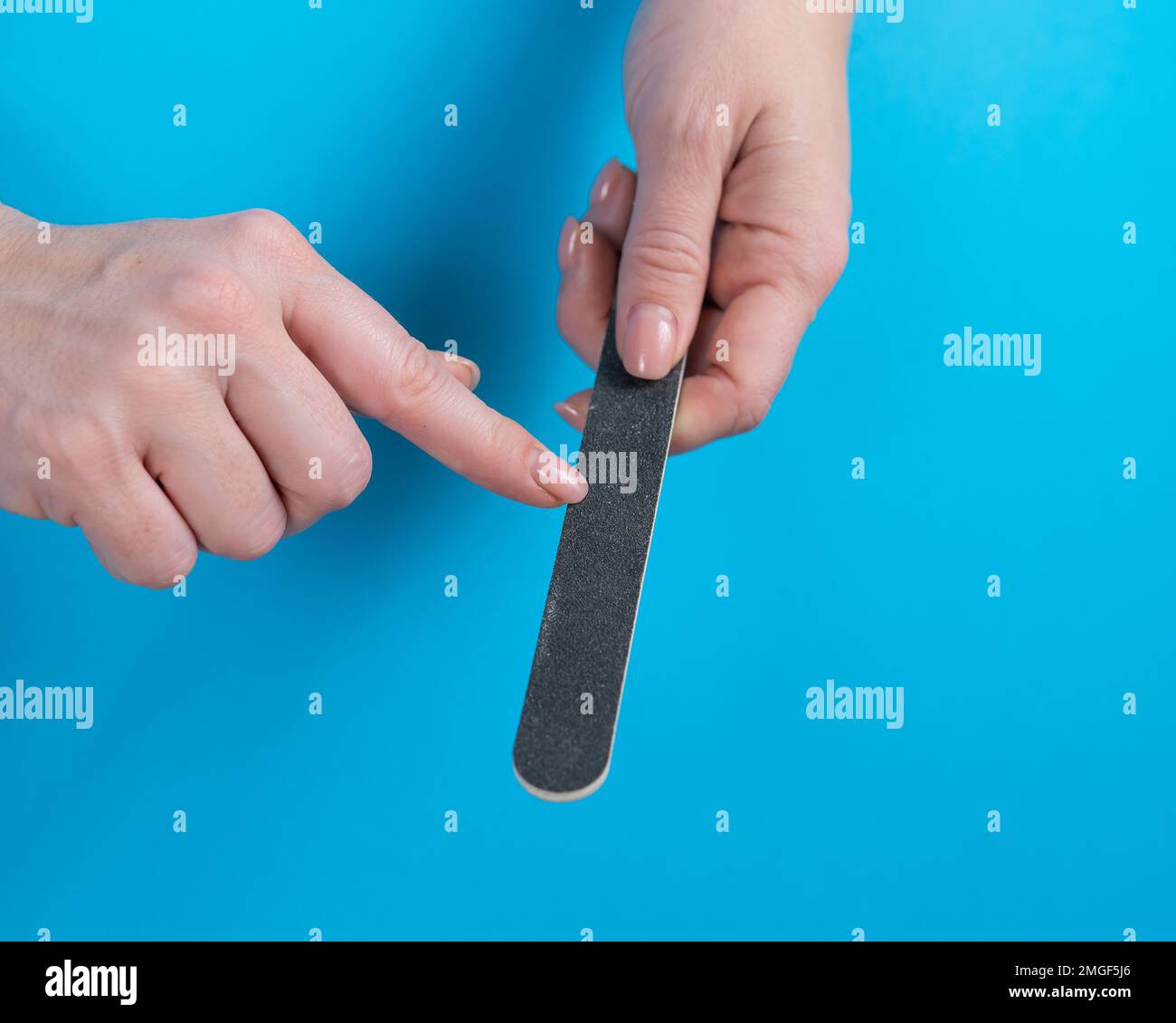 Donna che archivia le unghie su uno sfondo blu. Foto Stock