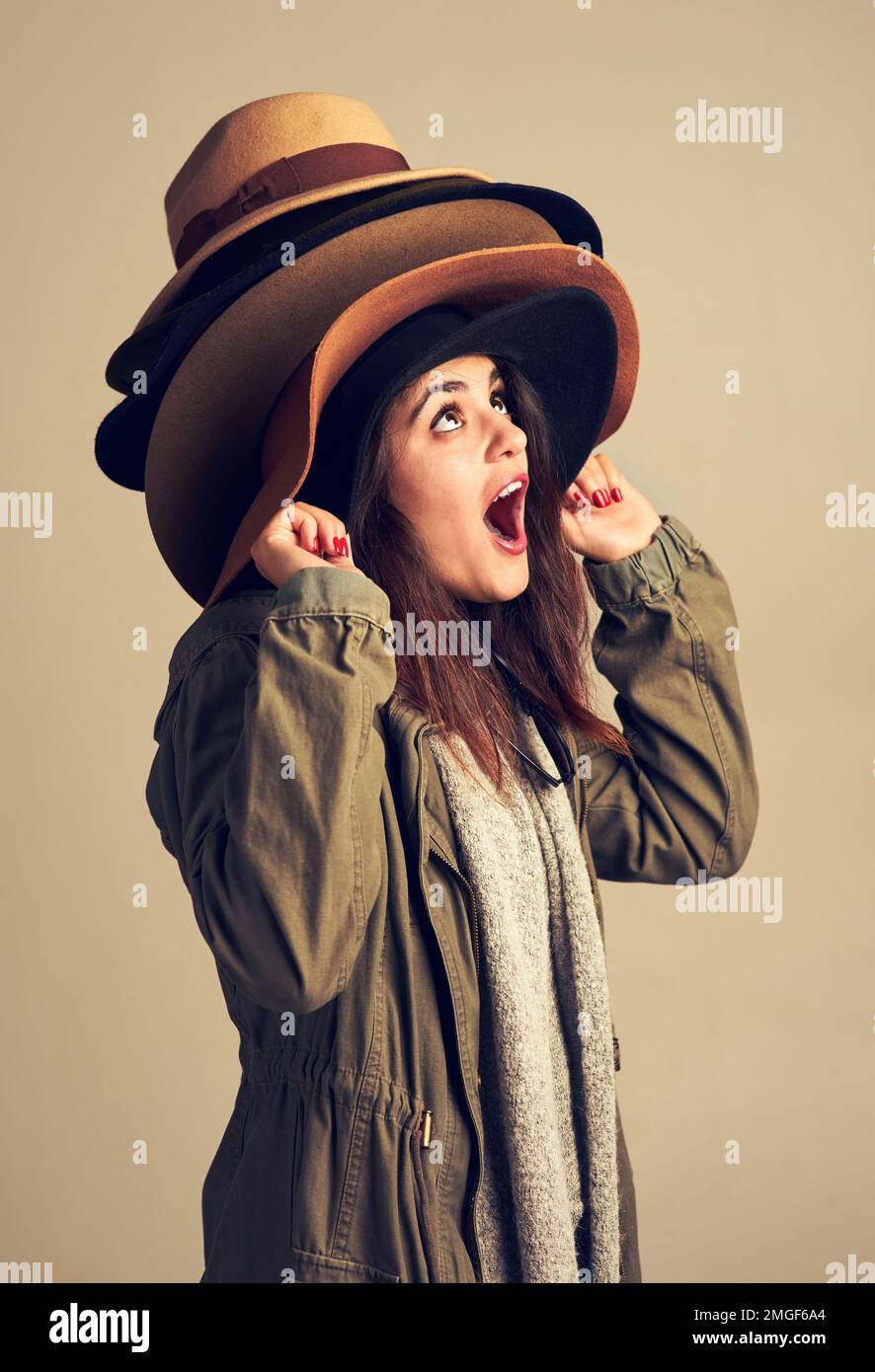 Theres un cappello differente per ogni occasione. Studio shot di una giovane donna che indossa un mucchio di cappelli su uno sfondo marrone. Foto Stock