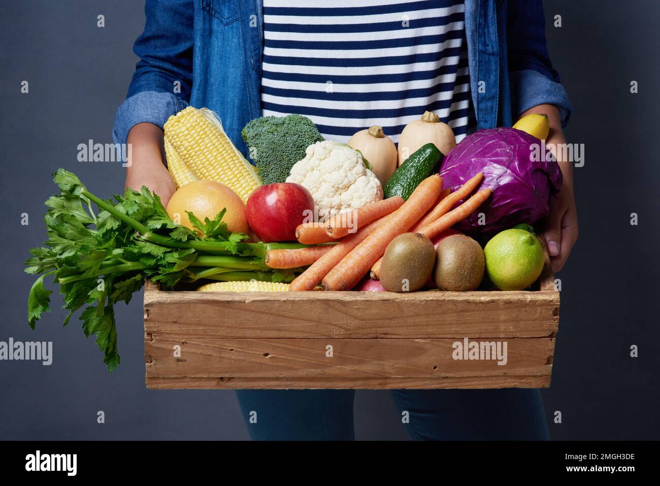Il mio tipo di fast food è costituito da verdure e frutta in entrata. Studio shot di una donna irriconoscibile che tiene una cassa di legno piena di frutta e verdura contro un Foto Stock Il mio tipo di fast food è costituito da verdure e frutta in entrata. Studio shot di una donna irriconoscibile che tiene una cassa di legno piena di frutta e verdura contro un Foto Stock