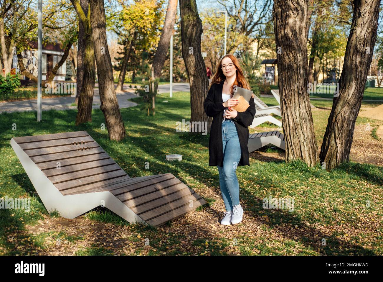 Scegliere un'università, un college. Studente universitario femminile con libri e computer portatile all'aperto. Ragazza studentessa del college Redhead con occhiali nel campus Foto Stock