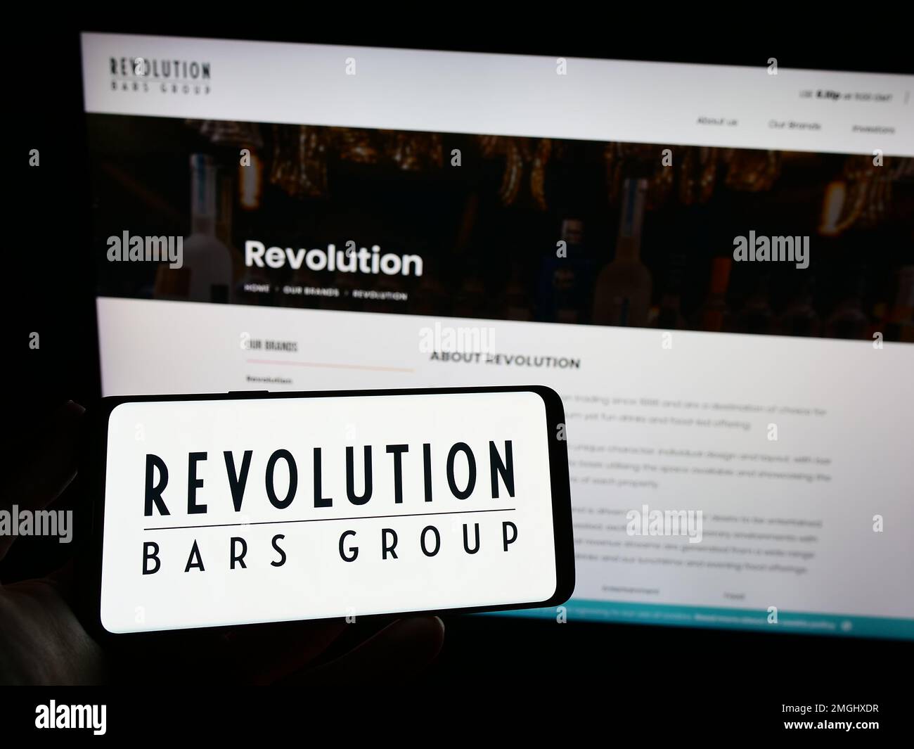 Persona in possesso di smartphone con il logo della società di ospitalità Revolution Bars Group plc sullo schermo di fronte al sito Web. Messa a fuoco sul display del telefono. Foto Stock