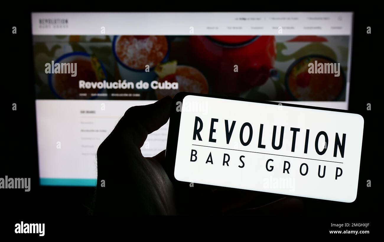 Persona che tiene il telefono cellulare con il logo della società di ospitalità Revolution Bars Group plc sullo schermo di fronte alla pagina web. Messa a fuoco sul display del telefono. Foto Stock