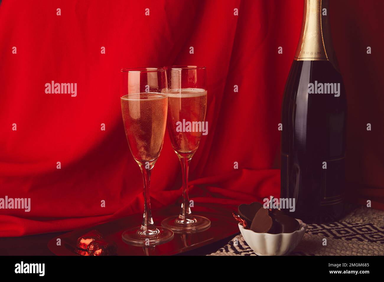 Tradizionale sfondo romantico di San Valentino con bottiglia di champagne, bicchieri, caramelle al cioccolato estetica Foto Stock