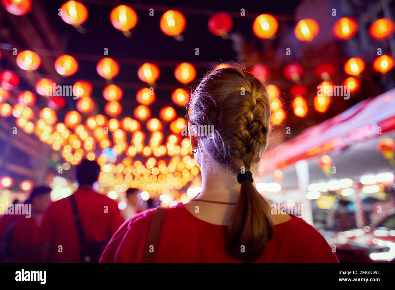Donna turistica in camicia rossa che guarda la decorazione del mercato notturno con le luci di lanterna rossa per il Capodanno cinese a Bangkok Chinatown in Thailandia Foto Stock