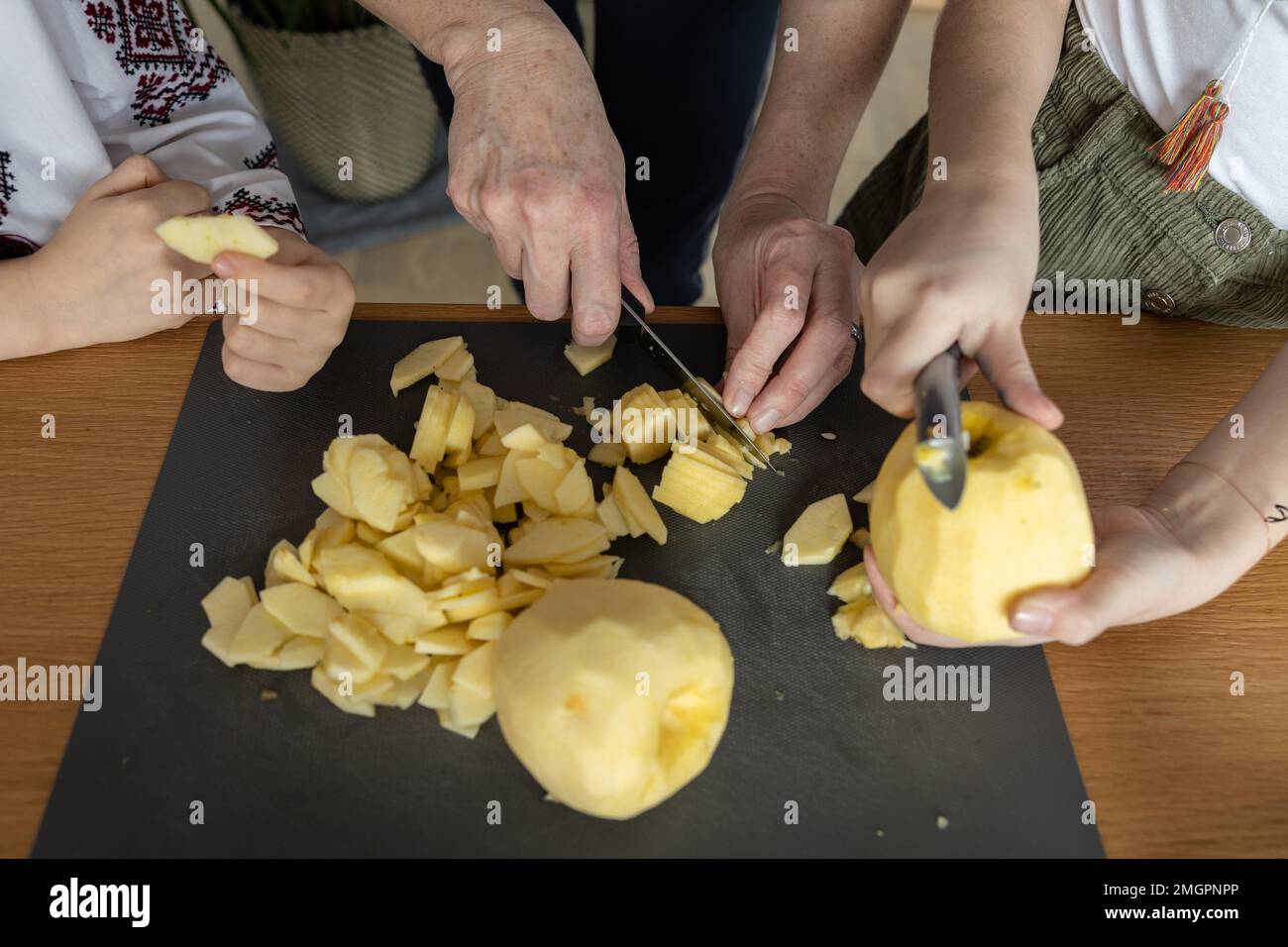 Mamma e 2 figlie sbucciare e tagliare le mele sul tavolo da cucina per fare una torta Foto Stock
