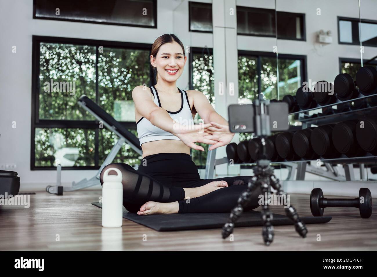 Allenamento femminile asiatico sul materassino yoga e con il telefono cellulare. Blogger sportivo femminile per la registrazione di video tramite smartphone. Esercitazione corso di formazione online Foto Stock