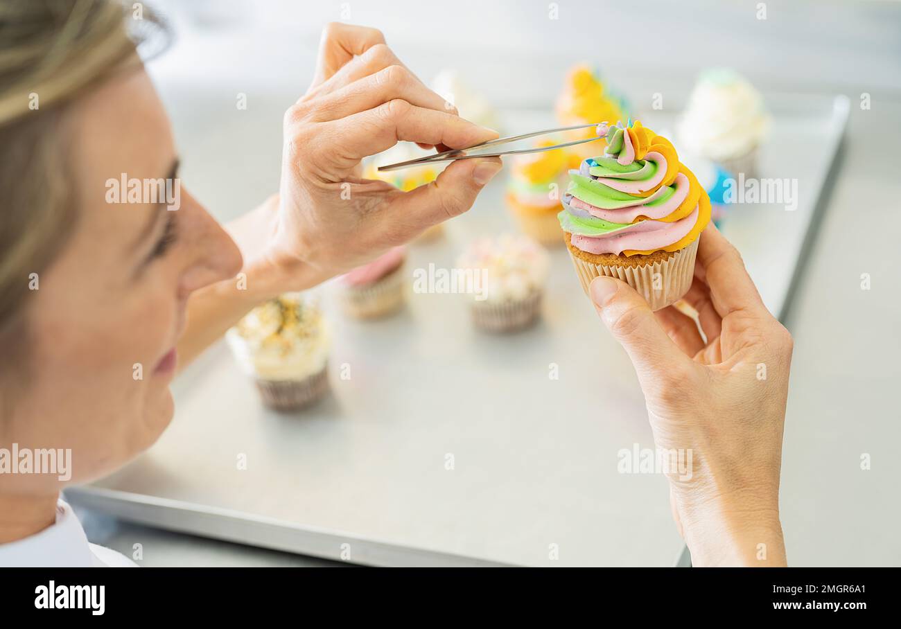 donne in pasticceria come pasticciere drappeggiato candy perla guarnizione su un muffin colorato con pinzette Foto Stock