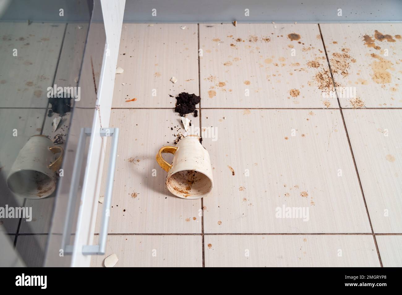 Tazza da tè rotta sul pavimento della cucina, tazza da caffè schiacciata e caffè macinato su tutte le piastrelle. Foto Stock