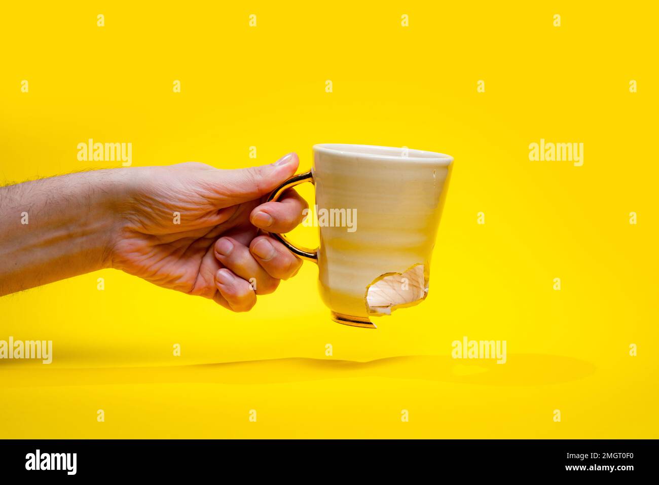 Uomo che tiene rotto tè tazza isolato su sfondo giallo. Primo piano del braccio che tiene la tazza di caffè incrinata Foto Stock