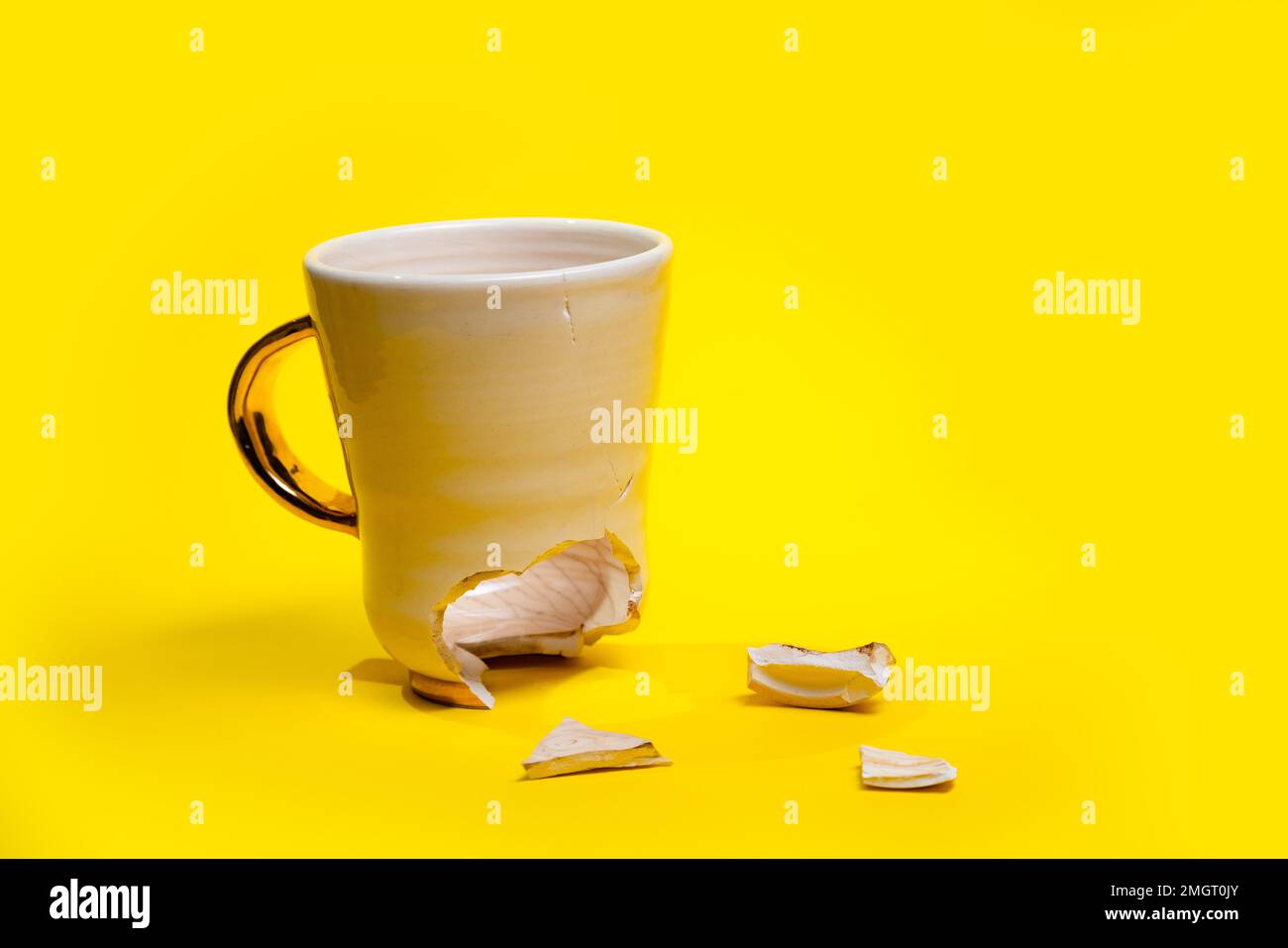Tazza da tè rotta isolata su sfondo giallo. Tazza di caffè incrinata e fragili pezzi in ceramica Foto Stock