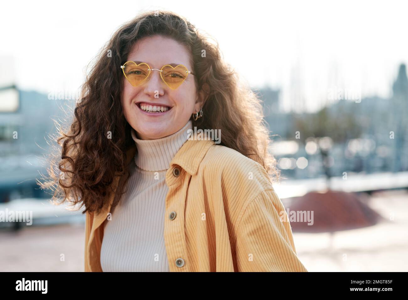 Donna con occhiali da sole che guarda la macchina fotografica e sorridente mentre si posa all'aperto. Foto Stock