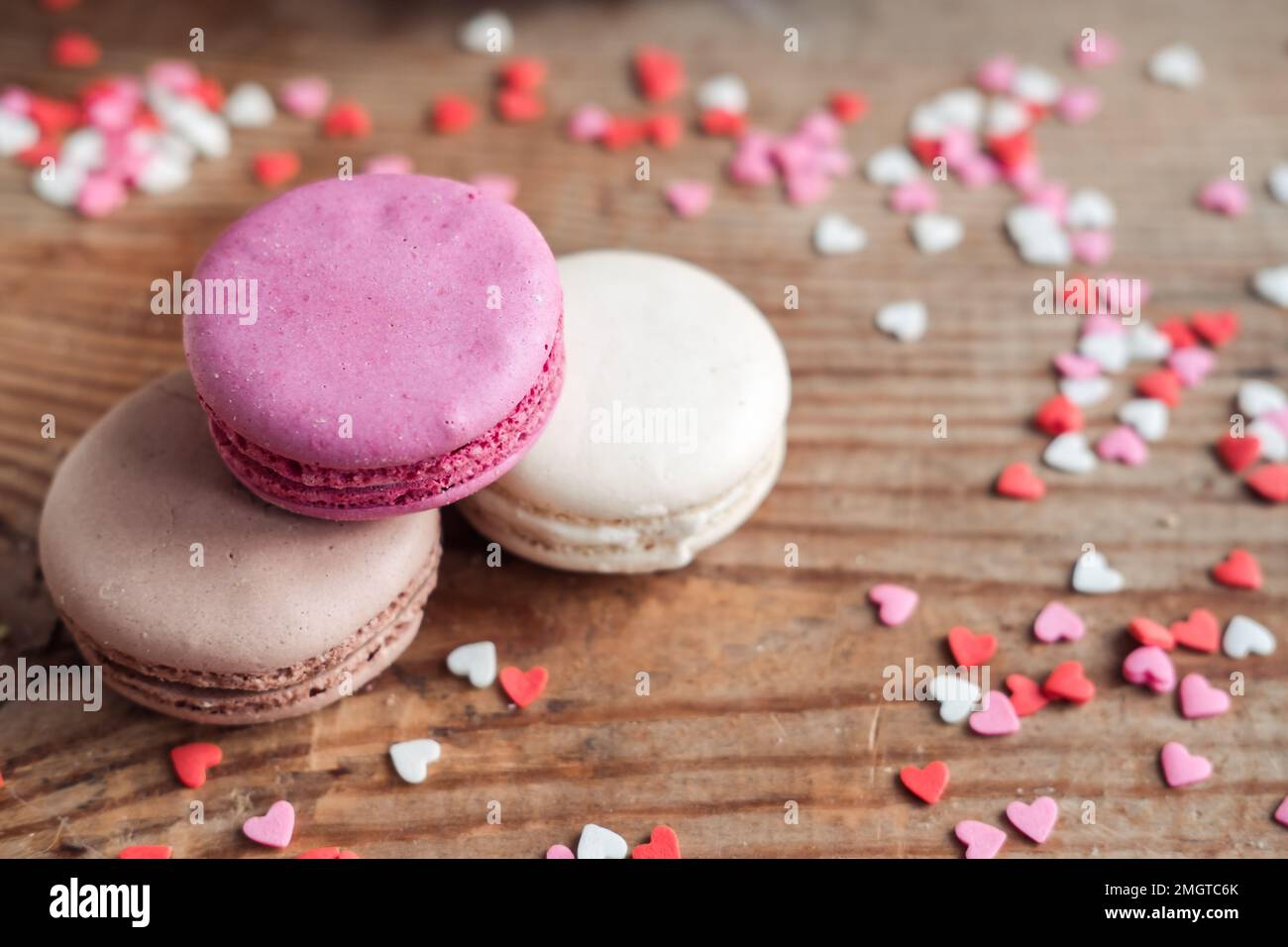 Macarone assortito cosparso di piccoli cuori su uno sfondo di legno, vista dall'alto Foto Stock