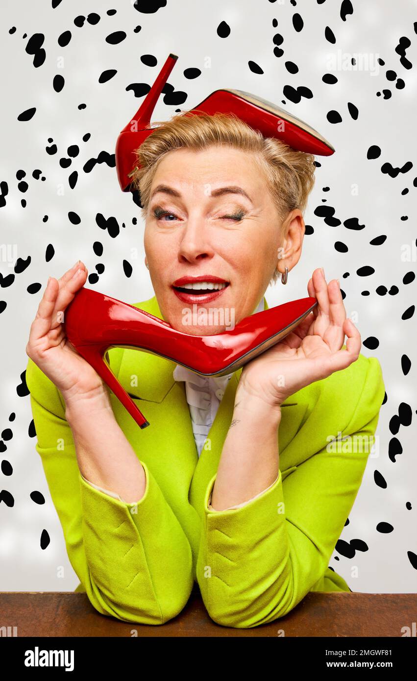 Bella donna bionda alla moda di mezza età con taglio corto con scarpe con tacchi rossi sullo sfondo della stampa dalmata. Foto Stock