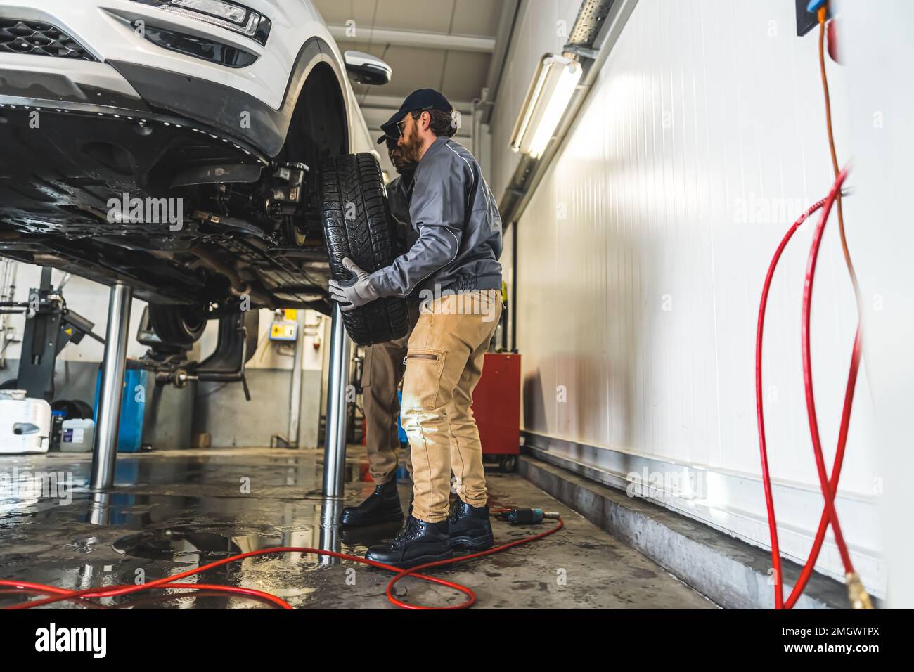 I meccanici dell'automobile sono occupati sostituire le ruote di un'automobile sull'ascensore in un negozio di riparazione auto. Foto di alta qualità Foto Stock