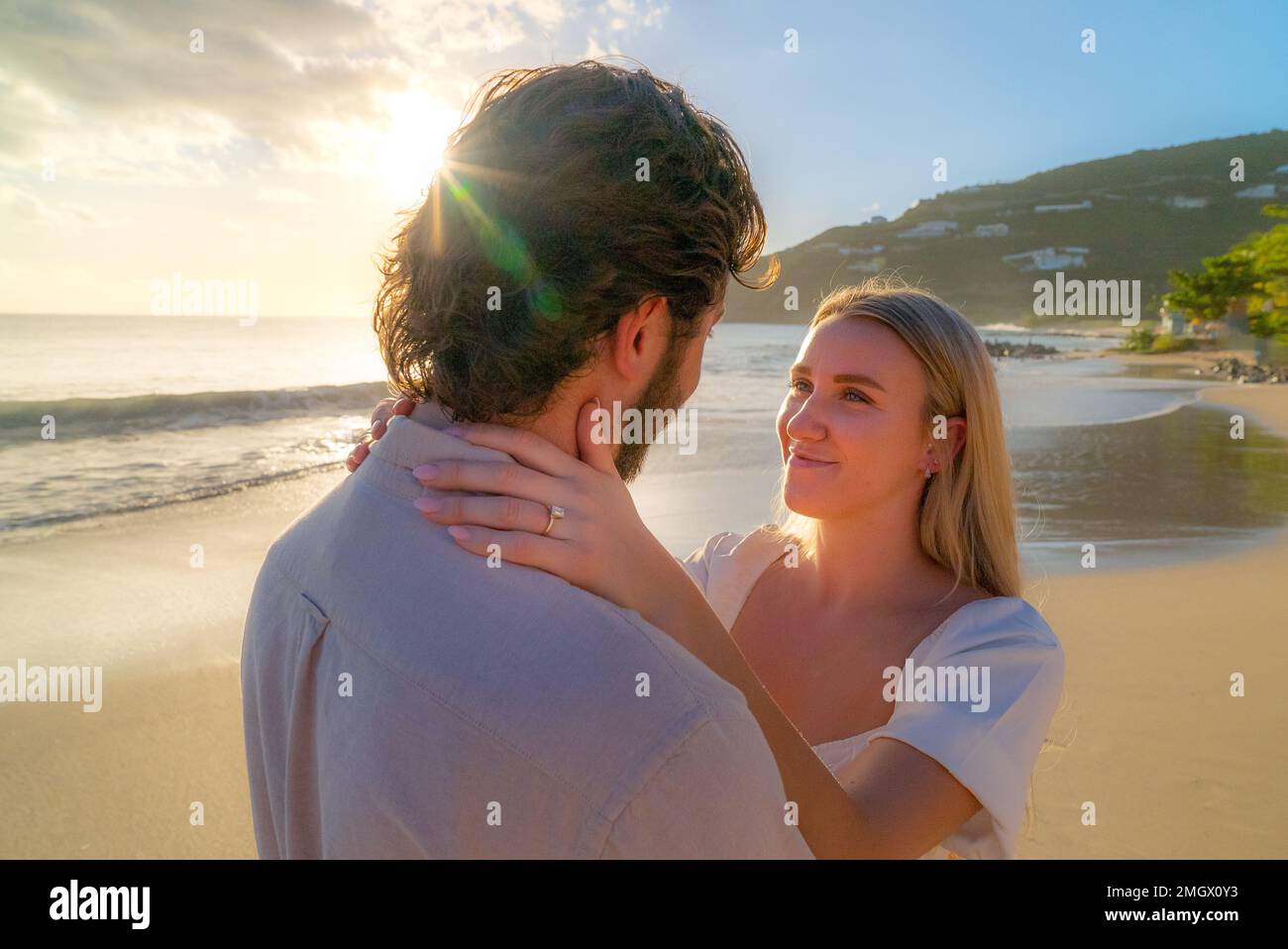 Coppia appena impegnata godendo di un romantico abbraccio durante l'ora d'oro su una spiaggia di sabbia vuota Foto Stock