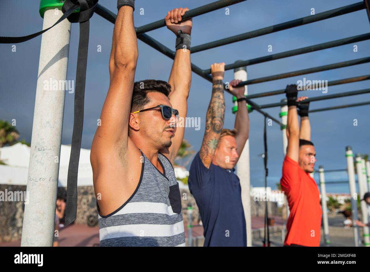 Tre uomini allenano facendo pull up in una palestra all'aperto, sport e stile di vita sano Foto Stock