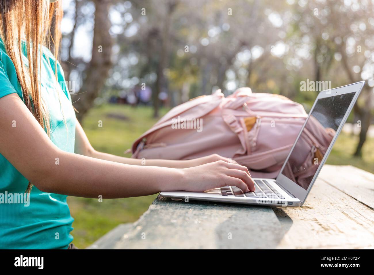 Studentessa universitaria irriconoscibile che studia, usa un computer portatile e si siede all'esterno in un parco Foto Stock