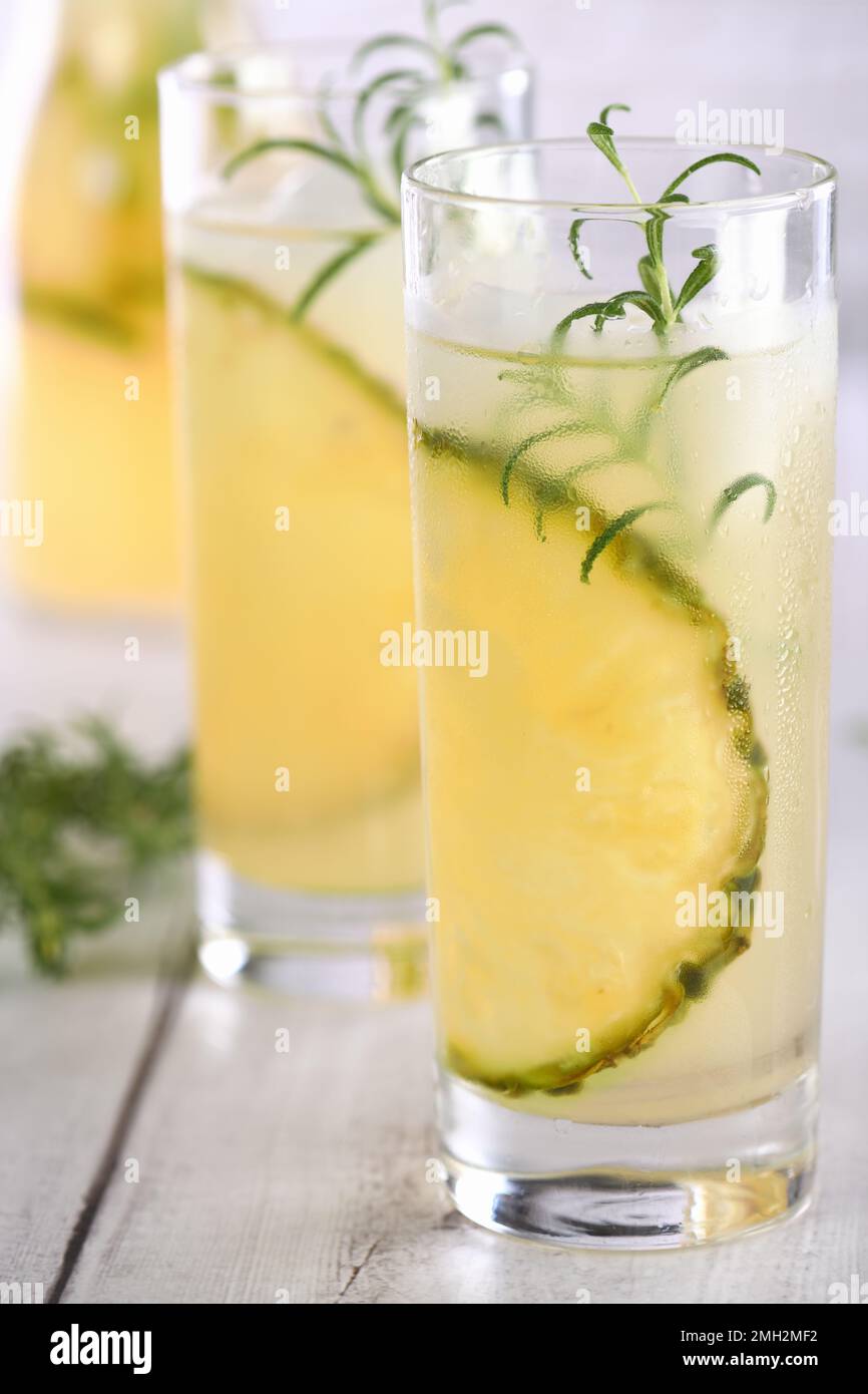 Un bicchiere di limonata con pezzi di ananas, cubetti di ghiaccio e rosmarino. Rinfresco cocktail biologico senza alcool. Foto Stock