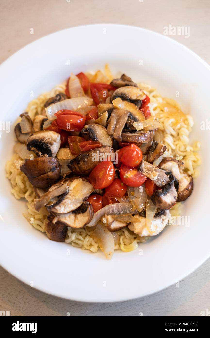 Friggere verdure, pomodori ciliegini, funghi e cipolla serviti con tagliatelle Raman condite. Foto Stock