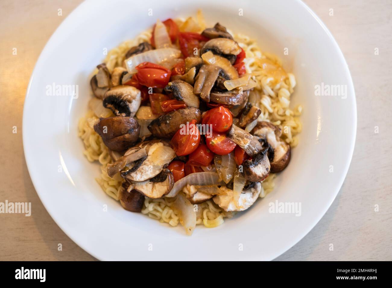 Friggere verdure, pomodori ciliegini, funghi e cipolla serviti con tagliatelle Raman condite. Foto Stock