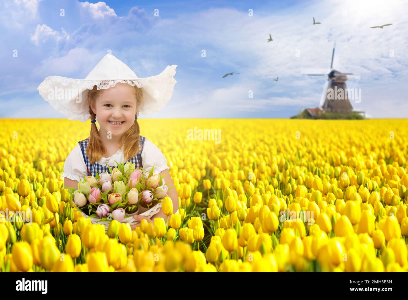 Bambino in campo di fiori di tulipano con mulino a vento in Olanda. Bambina olandese in costume tradizionale nazionale, vestito e cappello, con cesto di fiori. Foto Stock