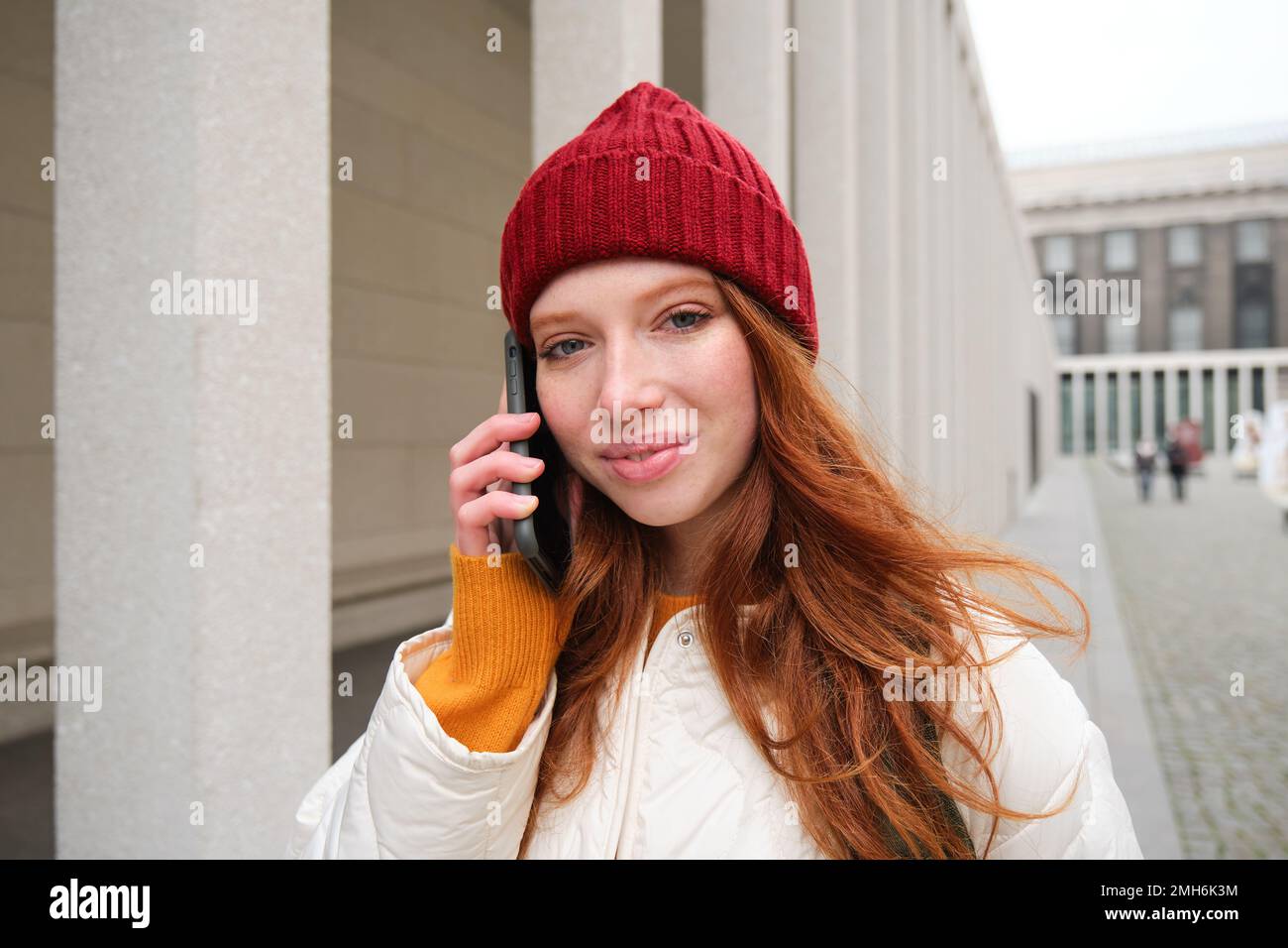 Banda larga mobile e persone. Sorridente giovane donna rossa cammina in città e parla sul telefono cellulare, chiamando un amico su smartphone, utilizzando internet per fare Foto Stock