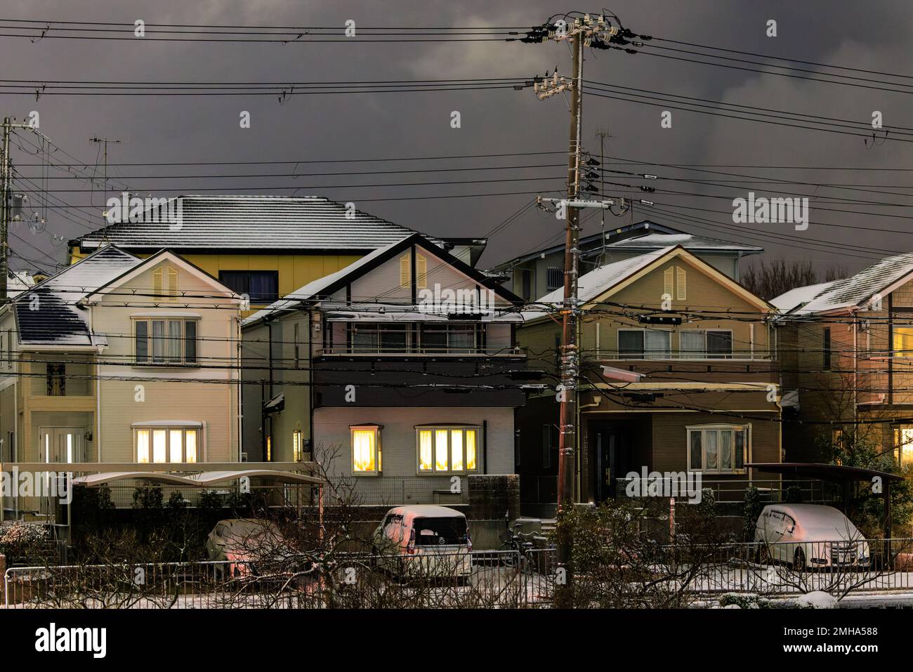 Polvere leggera di neve sulle case suburbane con le luci accese di notte Foto Stock