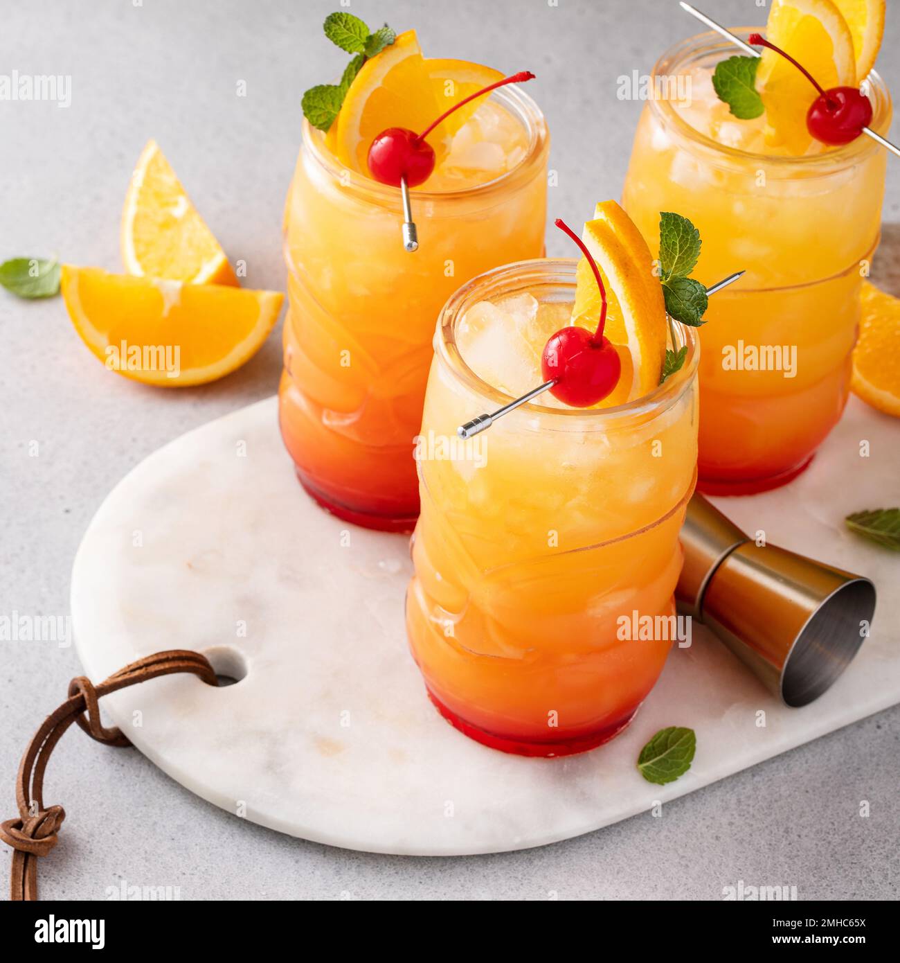 Punch al rum in bicchieri tiki con fette di arancia e ciliegia Foto Stock