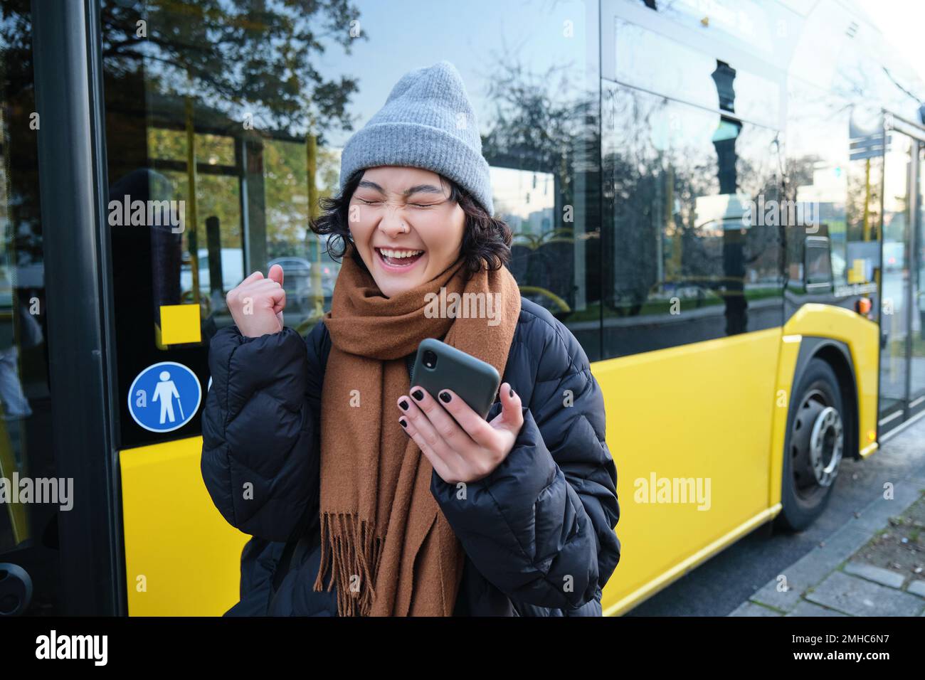 Persone moderne e stile di vita. Felice ragazza asiatica urla da gioia, festeggia, si trova vicino ai trasporti pubblici degli autobus e sembra stupito Foto Stock