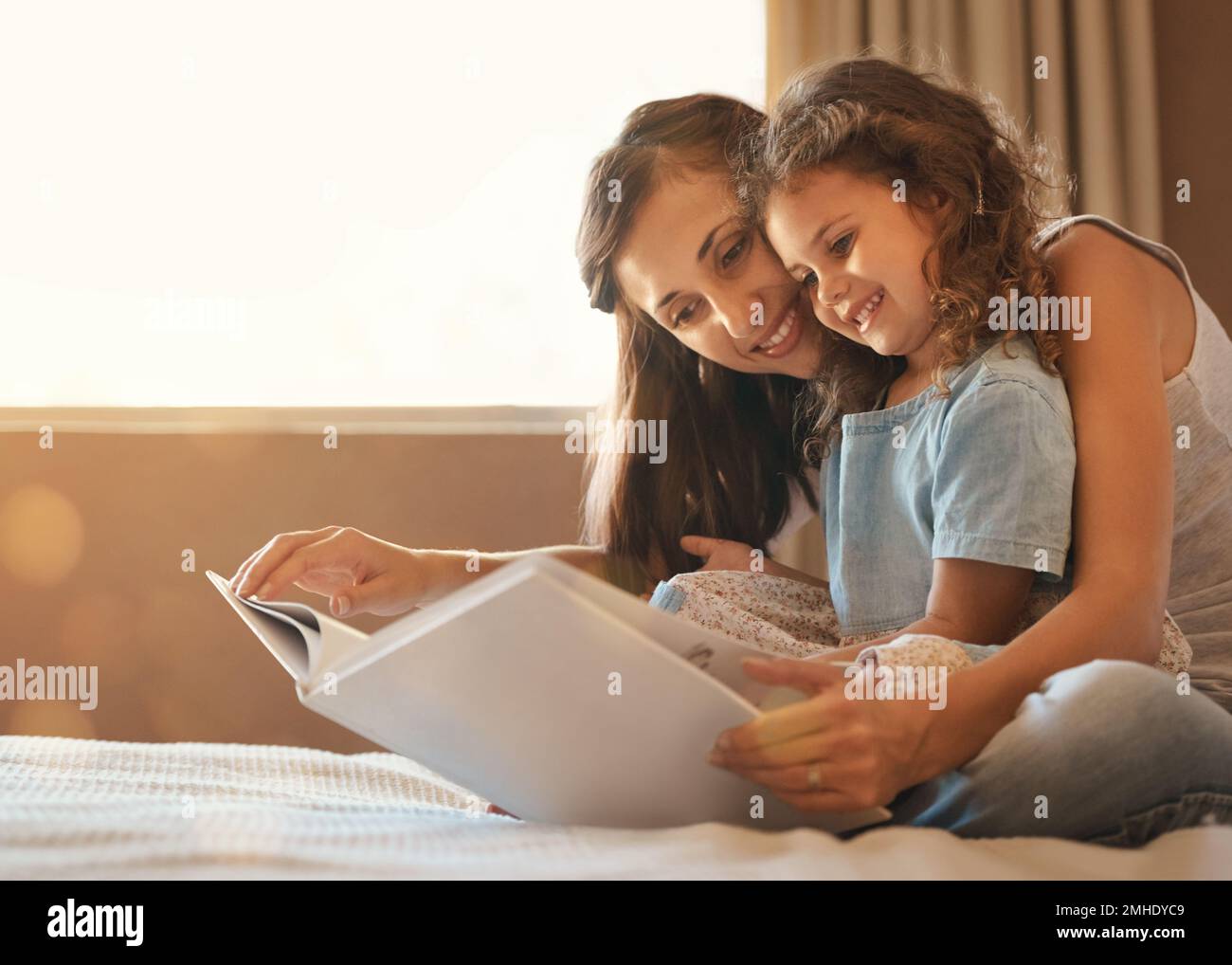 E vissero felici e contenti. una madre e una figlia felici a casa leggendo un libro di storia sul letto. Foto Stock