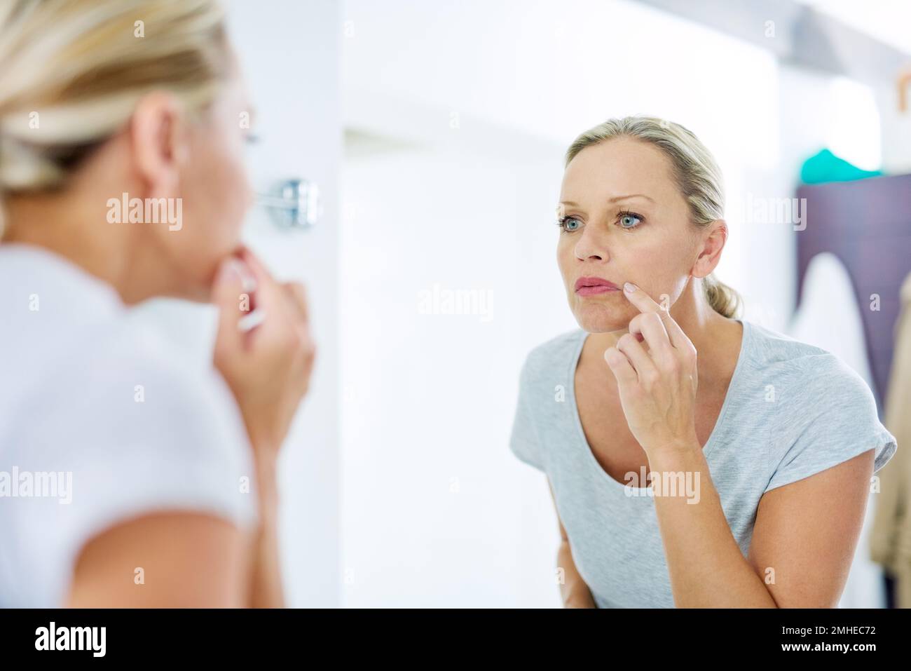 Ora è il momento di prendere cura della vostra pelle. una donna matura che ispeziona la pelle di fronte allo specchio del bagno. Foto Stock