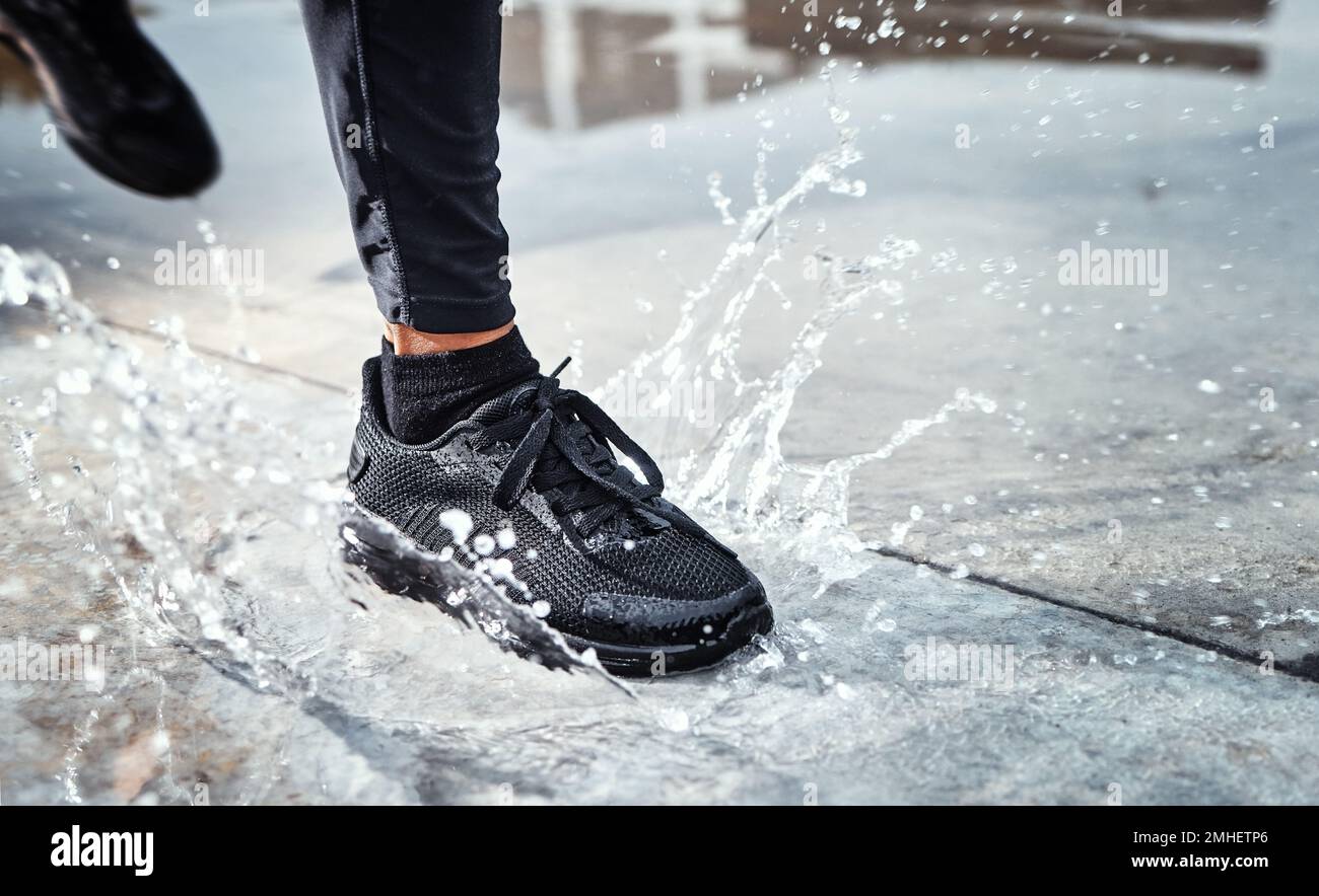 I piedi spruzzano l'acqua in strada, la persona che corre sotto la pioggia e le scarpe in pozzanghera di Seattle Road per il cardio all'aperto. Allenamento per i corridori per la maratona, continua Foto Stock
