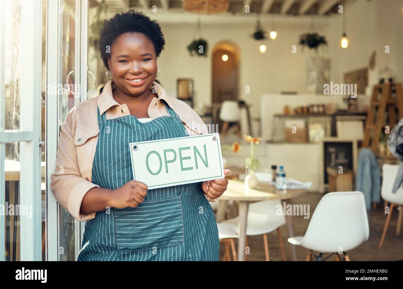 Open Sign, ritratto e black woman business startup in caffetteria, ristorante o negozio al dettaglio con un sorriso per il successo. Capo, manager o persona che tiene la mano Foto Stock