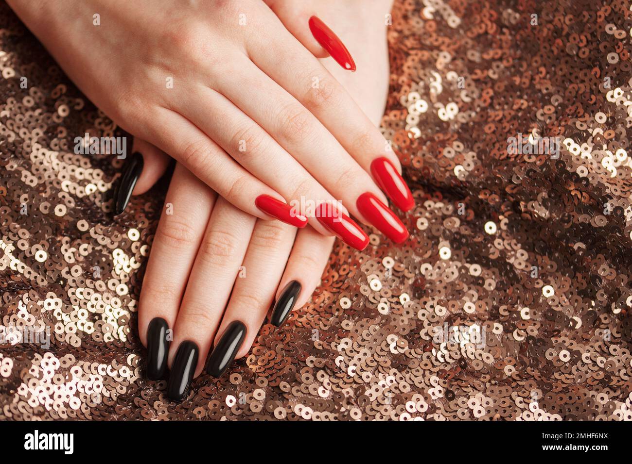 Mani di giovane ragazza con manicure rossa e nera sulle unghie su sfondo paillettes Foto Stock