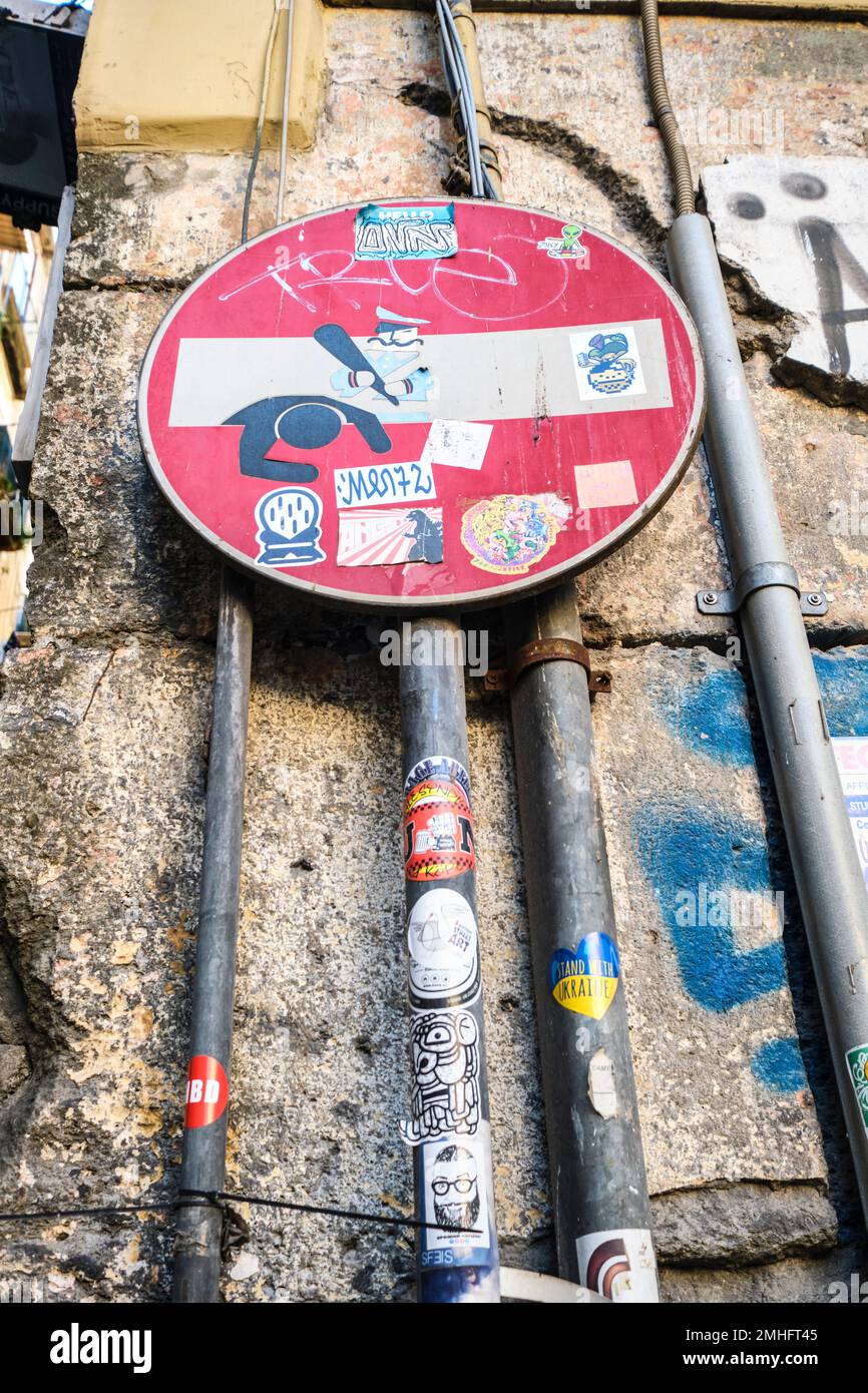 Una rotonda, rosso e bianco non entrare strada, cartello stradale. E' stato disfatto con adesivi che raffigurano una polizia che batte. Un esempio di grafitti a Napoli, Foto Stock