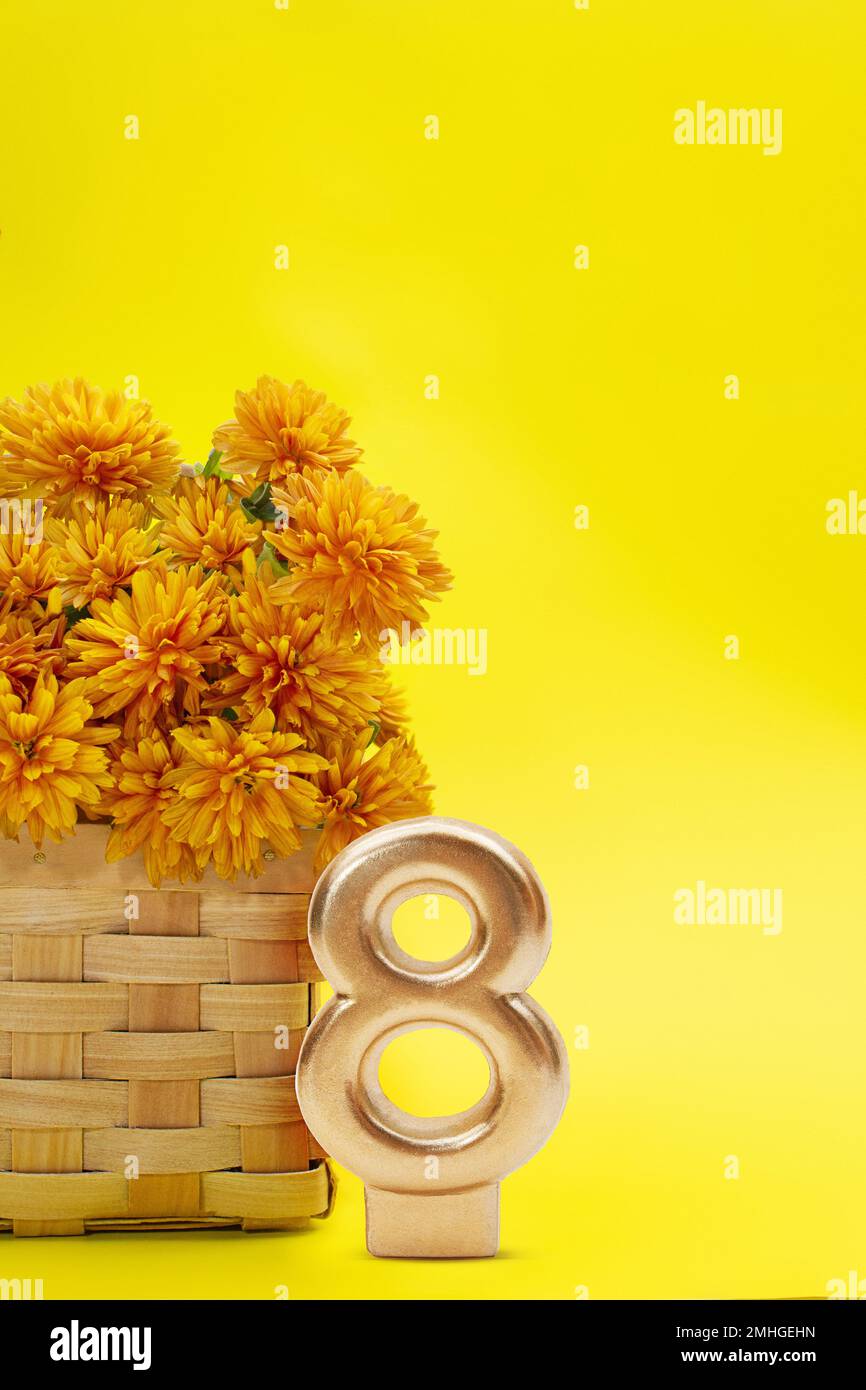 Crisantemi arancioni in cestello con numero 8 otto su sfondo giallo. Verticale. Giornata internazionale della donna, 8 marzo, compleanno. Spazio di copia Foto Stock