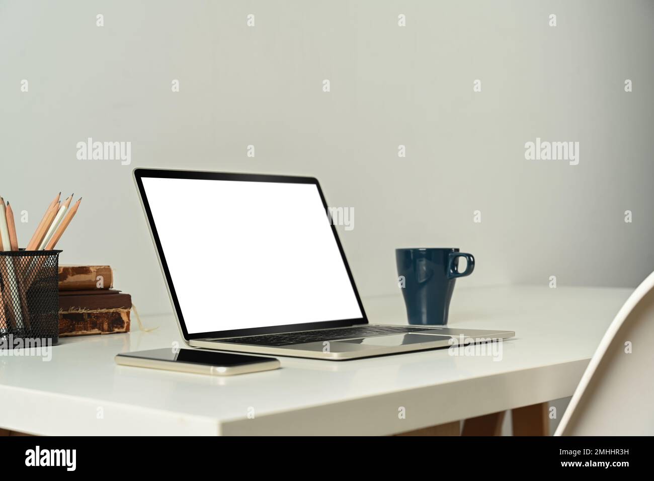 Computer portatile con schermo vuoto, tablet, libri e una tazza di caffè su un tavolo bianco Foto Stock